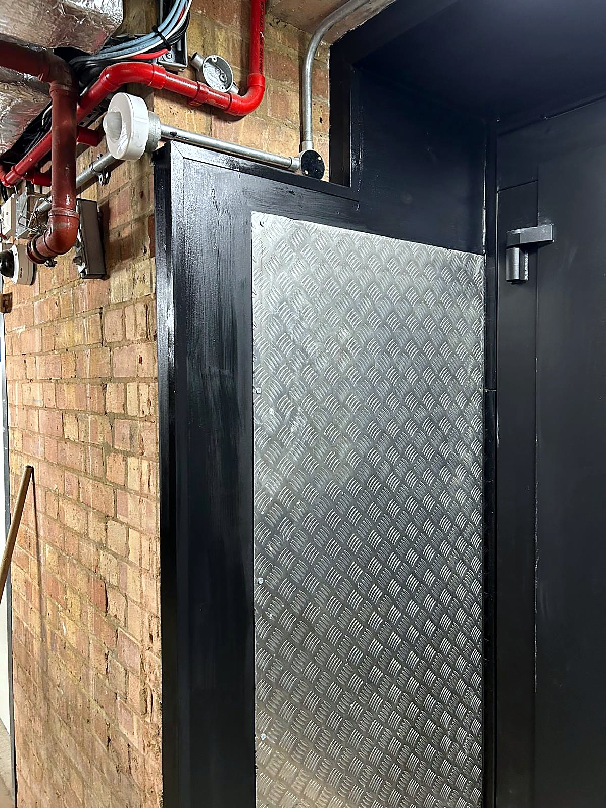 Traction goods lift enclosure beside a brick wall