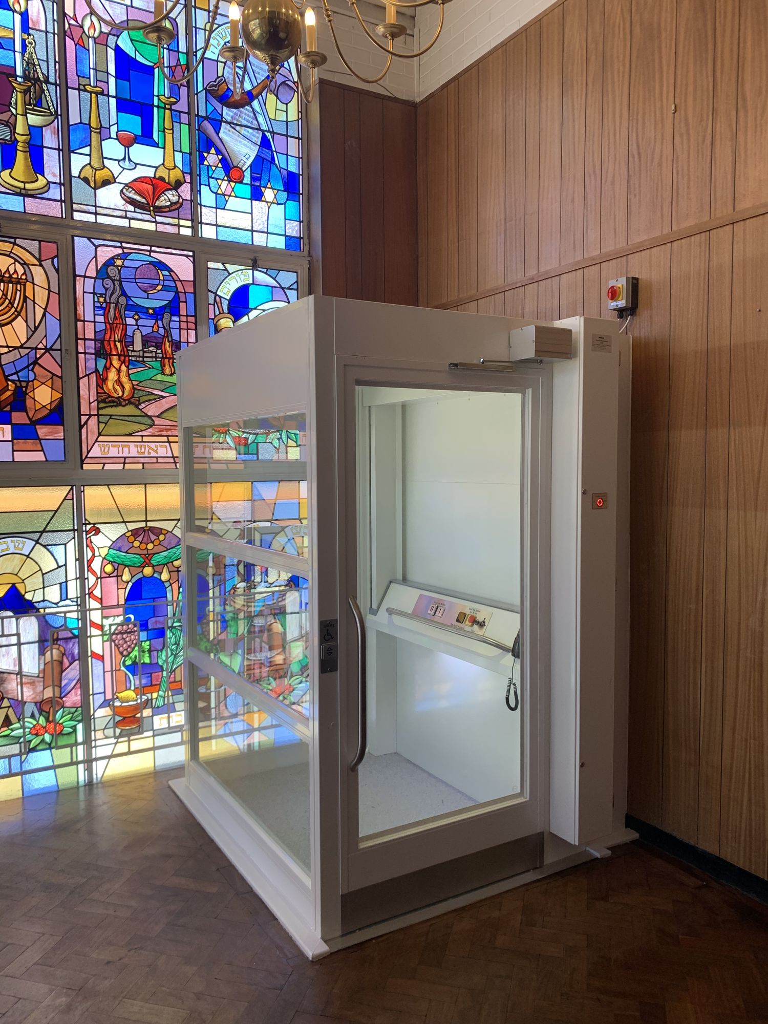 Glazed platform lift enclosure in front of a stained glass window